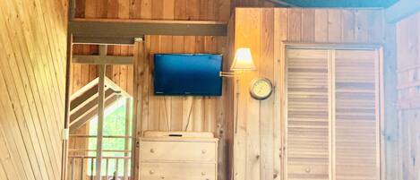 A wooden interior with a television mounted on the wall, a clock, and a wooden cabinet.