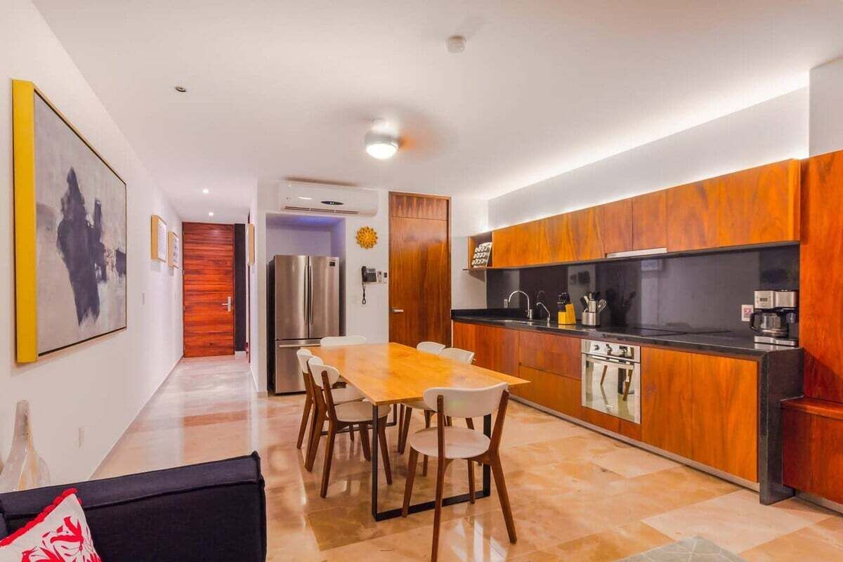 Une cuisine moderne avec des meubles en bois, un réfrigérateur en acier inoxydable et un coin repas comprenant une table et des chaises en bois.