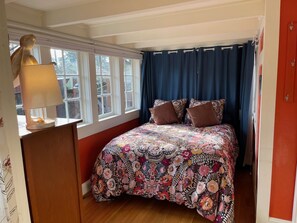 Une chambre à coucher avec une couvre-lit à motifs floraux, une lampe de chevet et une fenêtre avec des rideaux.