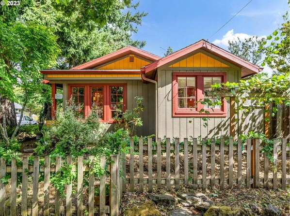 Une maison à deux étages, avec une clôture en bois à l’avant, entourée de verdure.