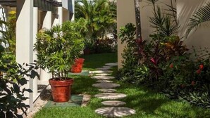 A narrow pathway flanked by buildings with balconies and palm trees, leading to a building with a clock. - Great 1BR Condo w/ Pool, Near Beach! AC! (Playa Del Carmen)