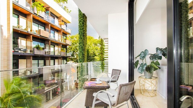 Un balcon doté d’une balustrade en verre, une table avec des chaises et des plantes en pot.