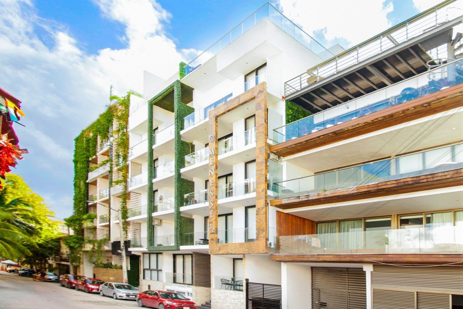 Un edificio residenziale moderno a più piani con balconi, un'area di parcheggio coperta e vista su una strada con auto parcheggiate.