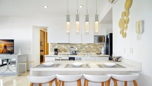 Une cuisine moderne dotée d’un îlot central, de tabourets de bar, de luminaires suspendus et d’un four à micro-ondes.