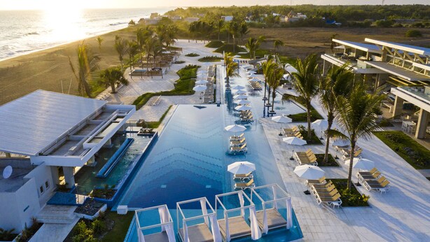 Un resort con piscina central, tumbonas y vista al mar.