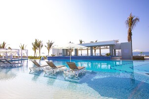 Zona de piscina con sillones reclinables, sombrillas y un edificio con vista al océano.