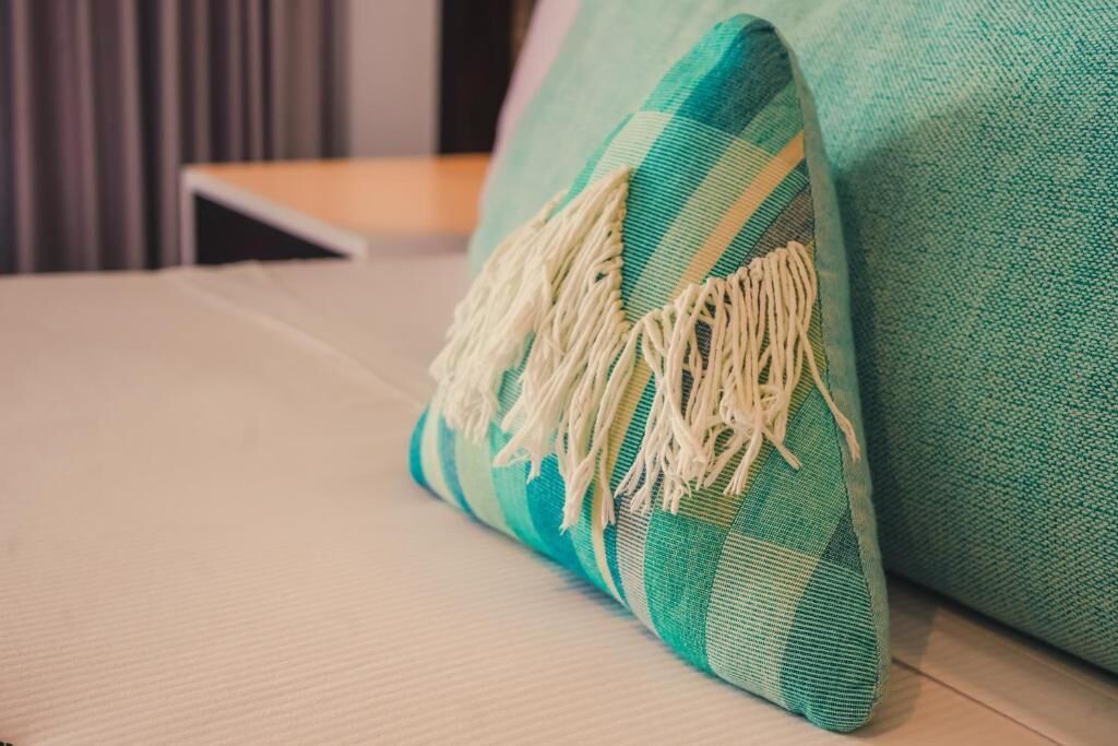 Un coussin à carreaux bleu sarcelle et blanc, orné de franges, posé sur un lit.