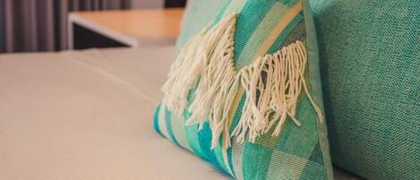Un coussin à carreaux bleu sarcelle et blanc, orné de franges, posé sur un lit.