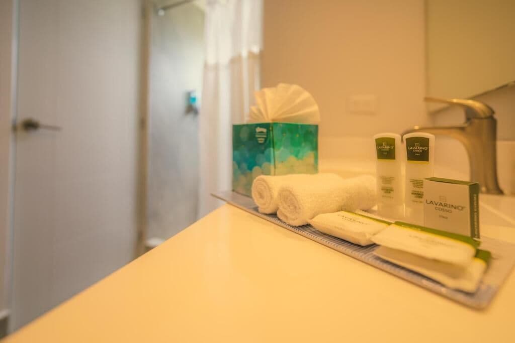 Un baño con un lavabo blanco, dos toallas enrolladas y dos botellas de jabón LAVARINO COSMO.