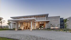 Un edificio moderno con entrada cubierta, amplias columnas y un jardín ajardinado.