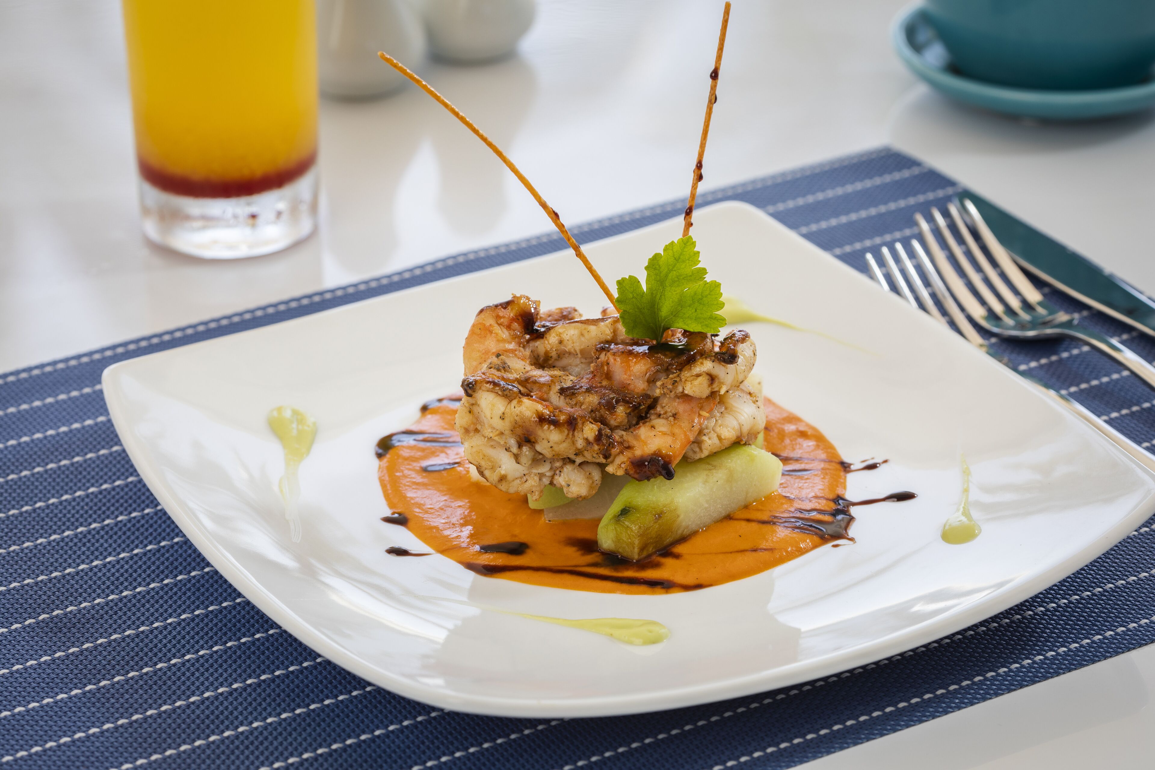A square white plate with a dish of food, a fork, and a knife on a blue striped placemat.