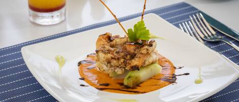 A square white plate with a dish of food, a fork, and a knife on a blue striped placemat.