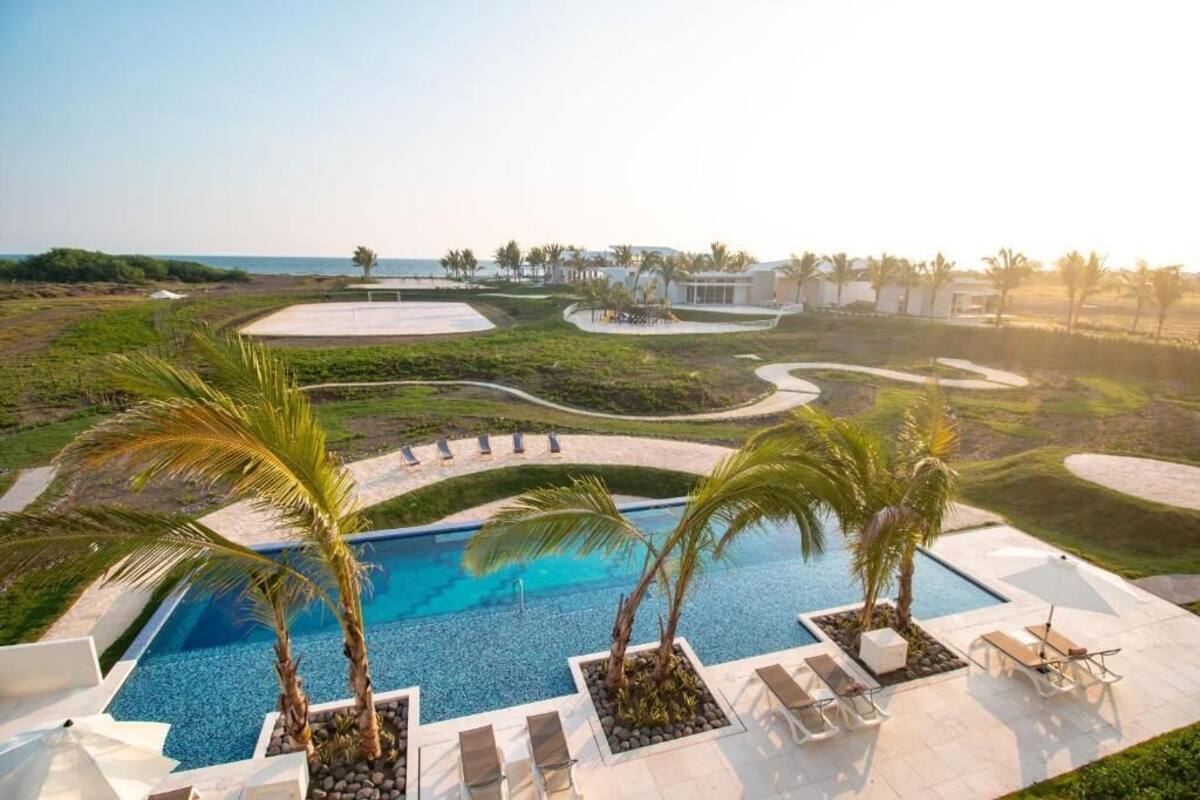 A pool area with palm trees, lounge chairs, and a view of the ocean.