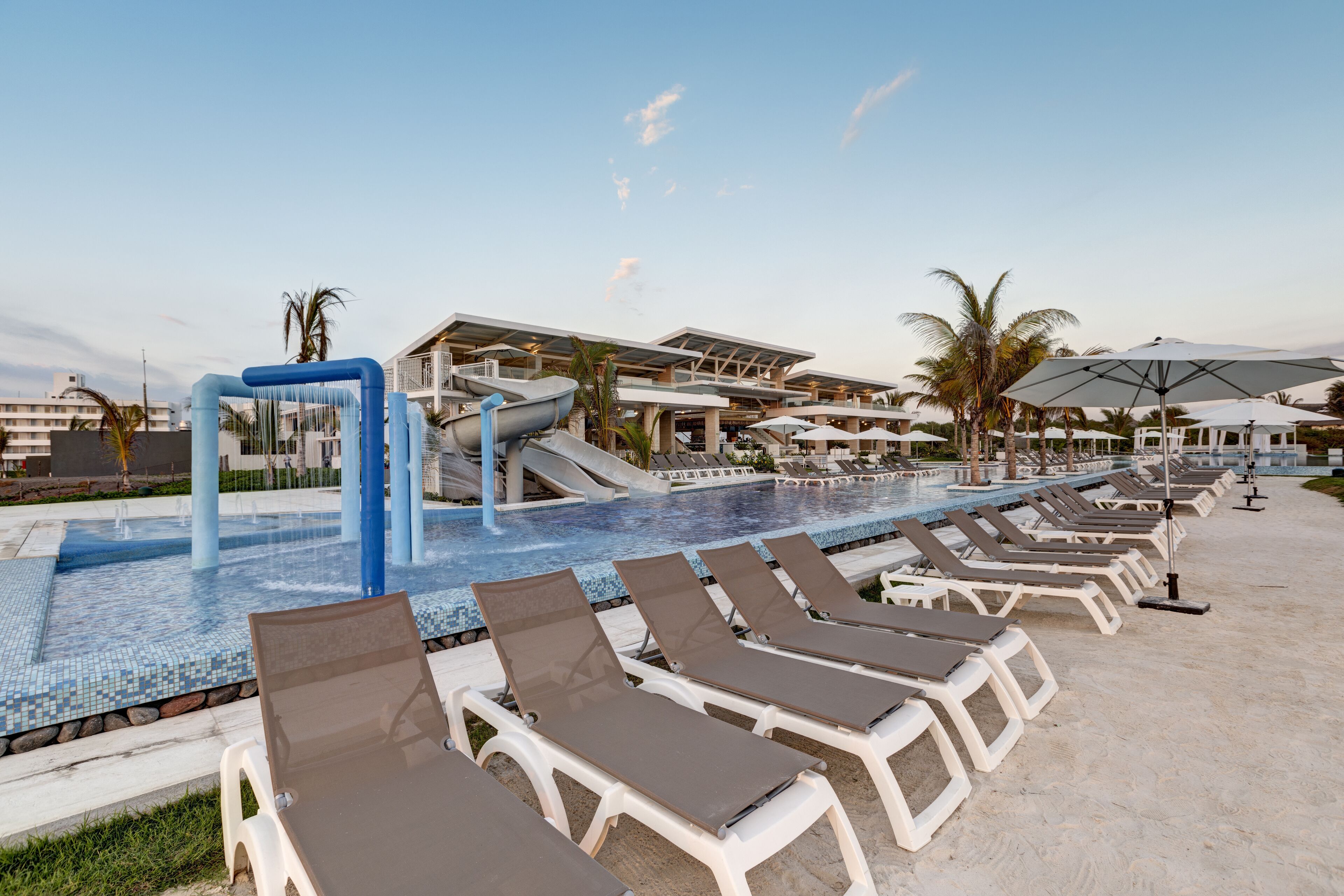 A pool area with lounge chairs, a water slide, and umbrellas.