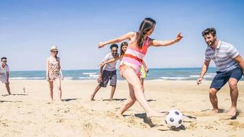 A group of people playing soccer on a sandy beach with the ocean in the background.