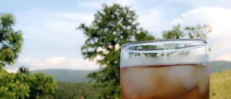 A glass of iced tea on a white wooden deck with a view of trees and hills in the background.