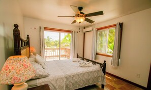 A bedroom with a bed, a ceiling fan, a nightstand with a lamp, and a window with curtains. - Chakra Le Esconddida House (San Pedro)