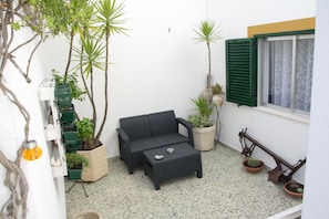 A small, enclosed outdoor space with a black sofa, a small table, and various potted plants.