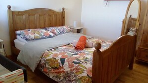 Una cama individual con ropa de cama floral, un cabecero de madera, una mesita de noche y un espejo en la pared.