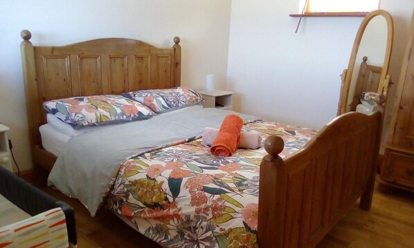 A single bed with floral bedding, a wooden headboard, a bedside table, and a mirror on the wall.