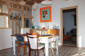 Un comedor con mesa y sillas de madera, una zona de cocina con electrodomésticos y un cuadro en la pared.