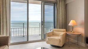 A room with a large sliding glass door leading to a balcony with a view of the ocean. There is a beige armchair and a small round table with a lamp. - Ocean Walk Resort (Daytona Beach)