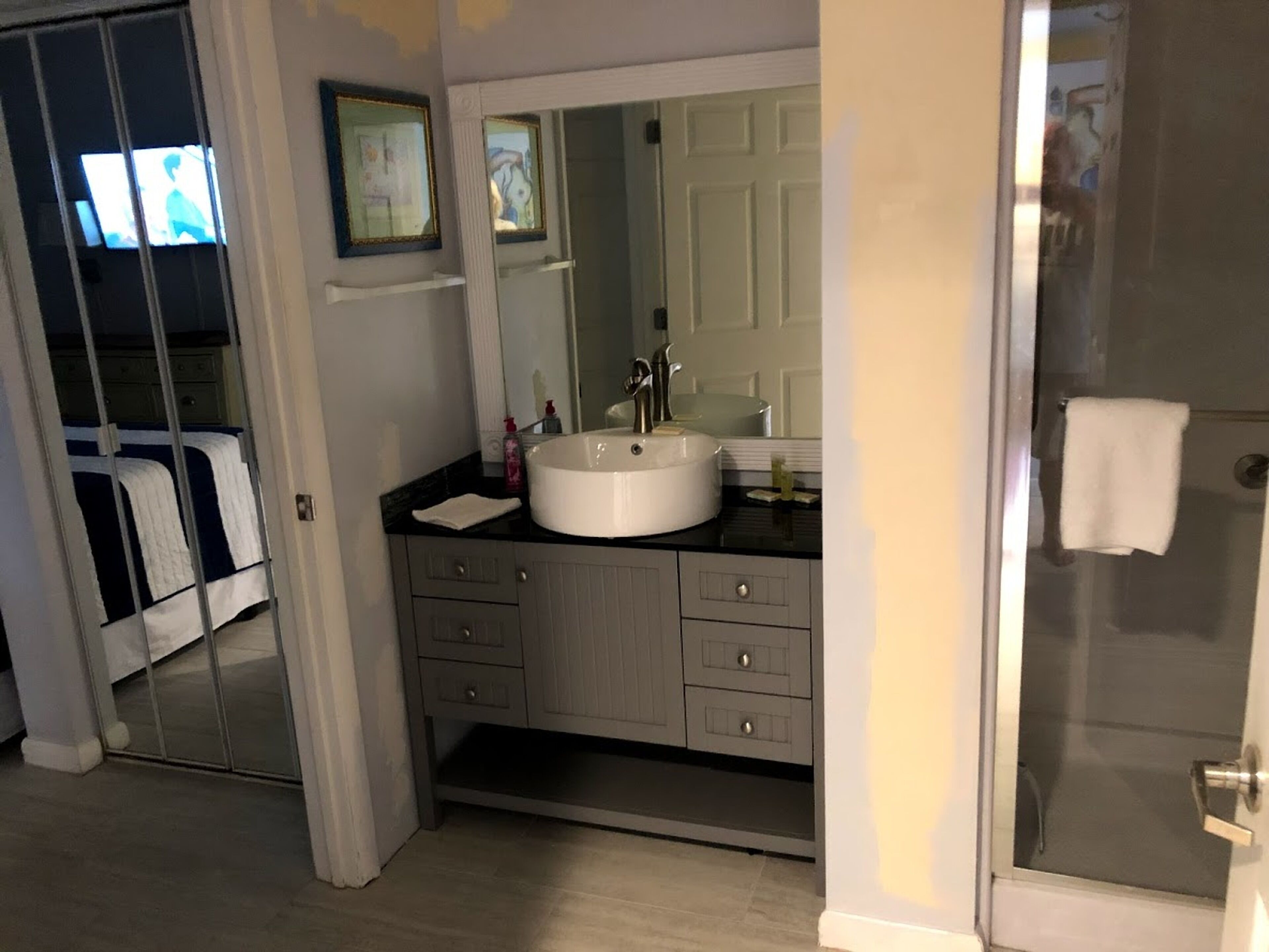 Casa de banho com lavatório branco, espelho e chuveiro. Uma toalha pendurada na porta do chuveiro.