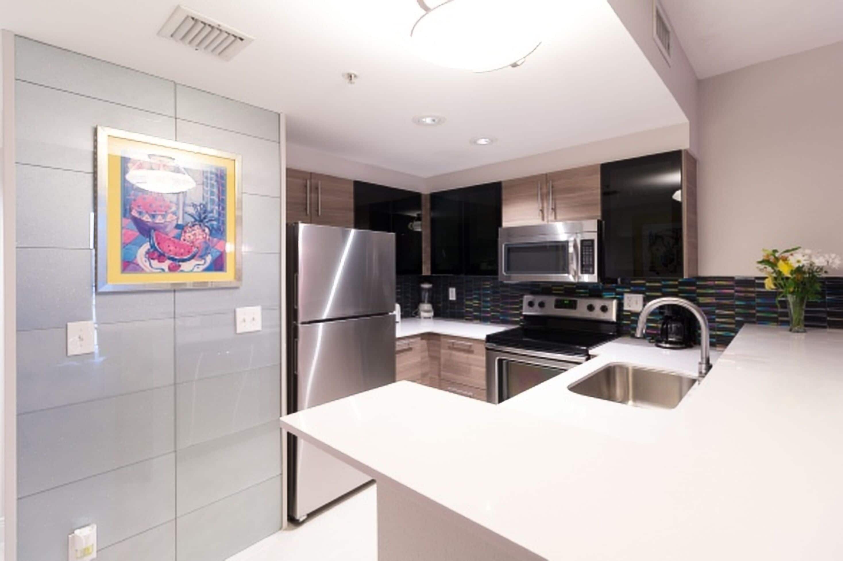 A modern kitchen with stainless steel appliances, a white countertop, and a colorful backsplash.