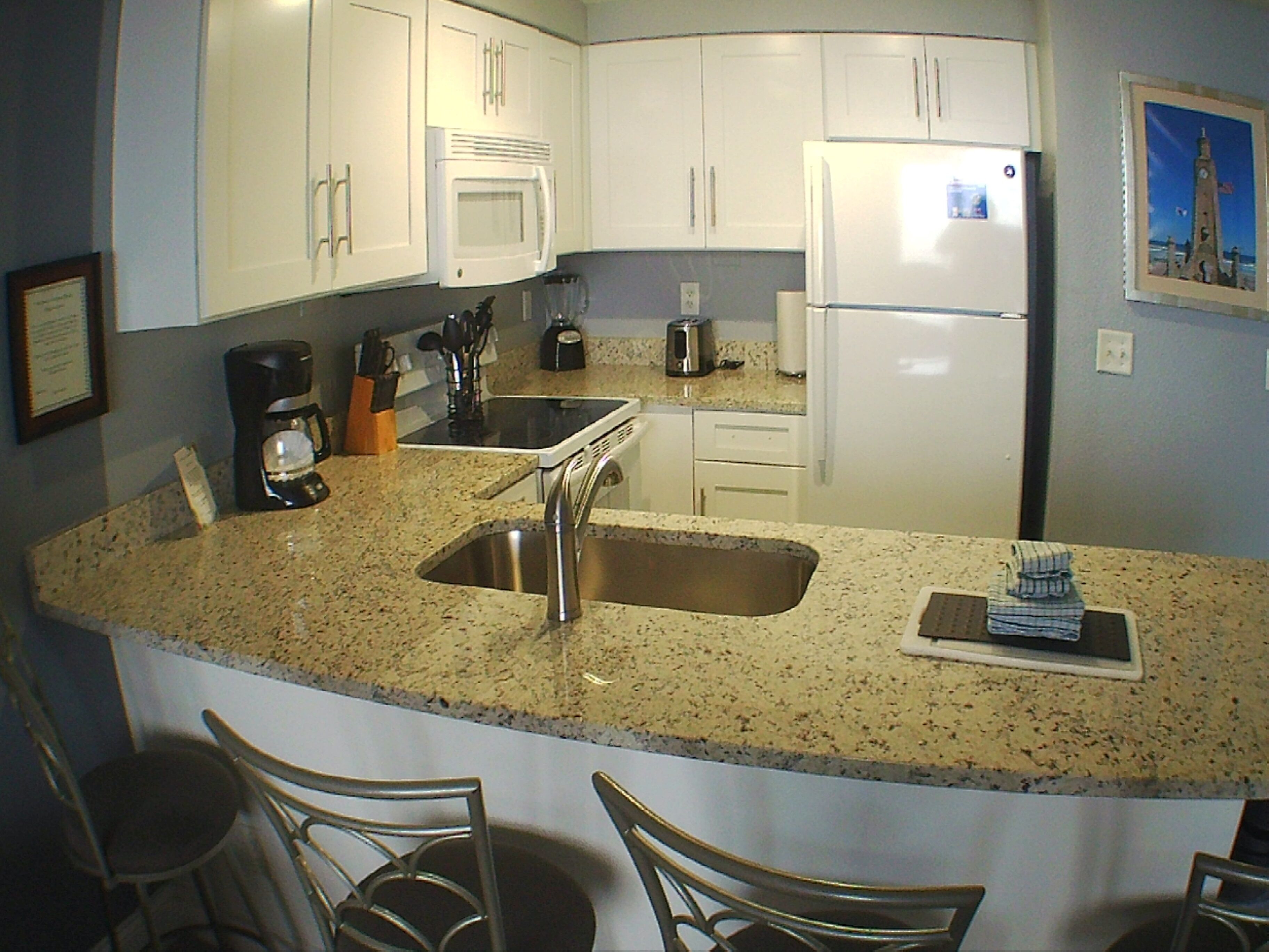 A kitchen with white cabinets, a stainless steel sink, a refrigerator, and a coffee maker.