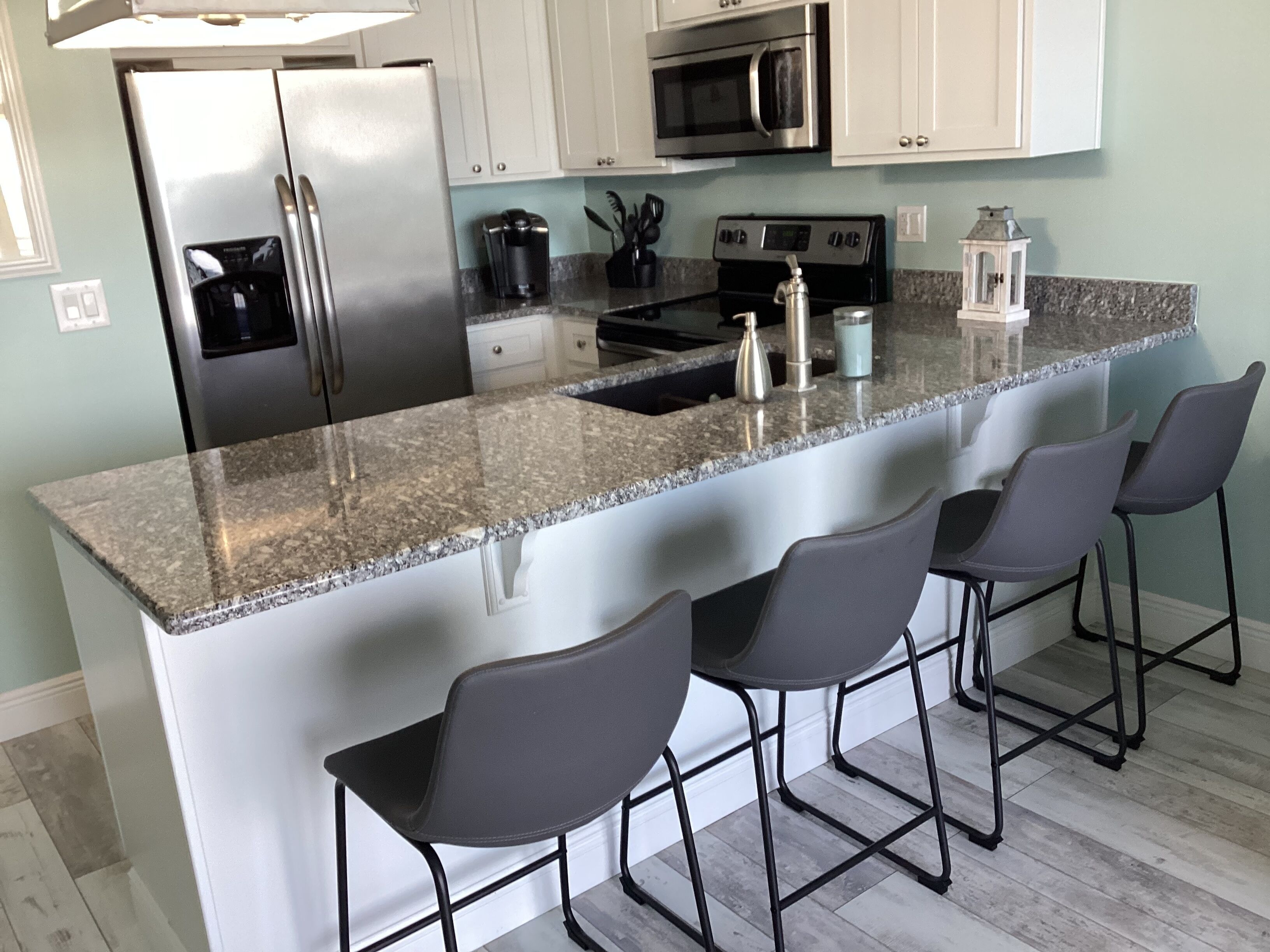 Una cocina con encimera de granito, electrodomésticos de acero inoxidable y cuatro taburetes de bar.