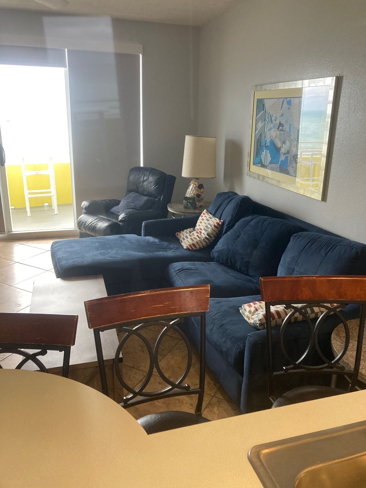 Una sala de estar con un sofá azul, una mesa de centro de madera, un sillón negro y una lámpara sobre una mesita auxiliar.