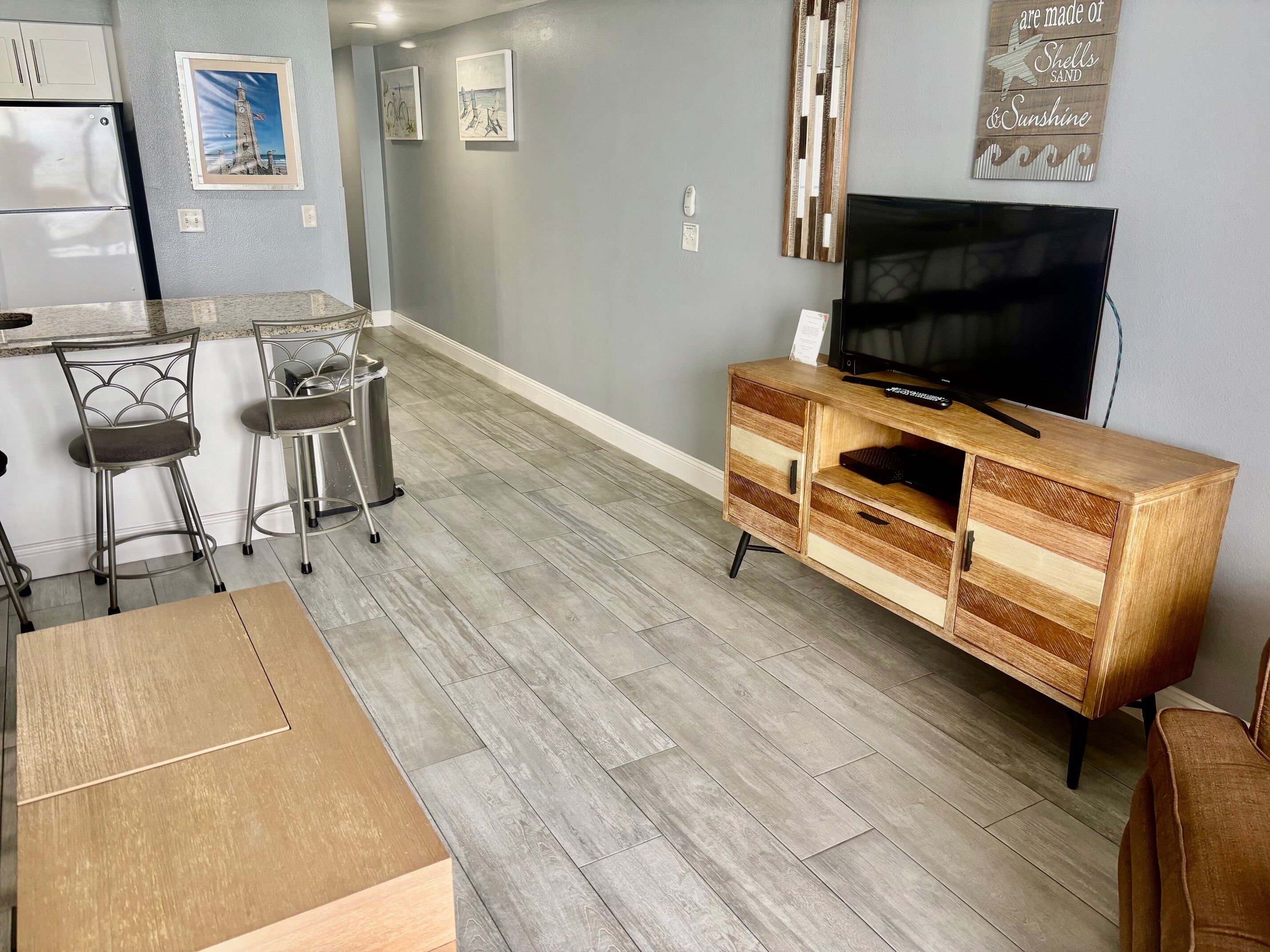 A modern kitchen with a refrigerator, bar stools, and a wooden cabinet with a TV.