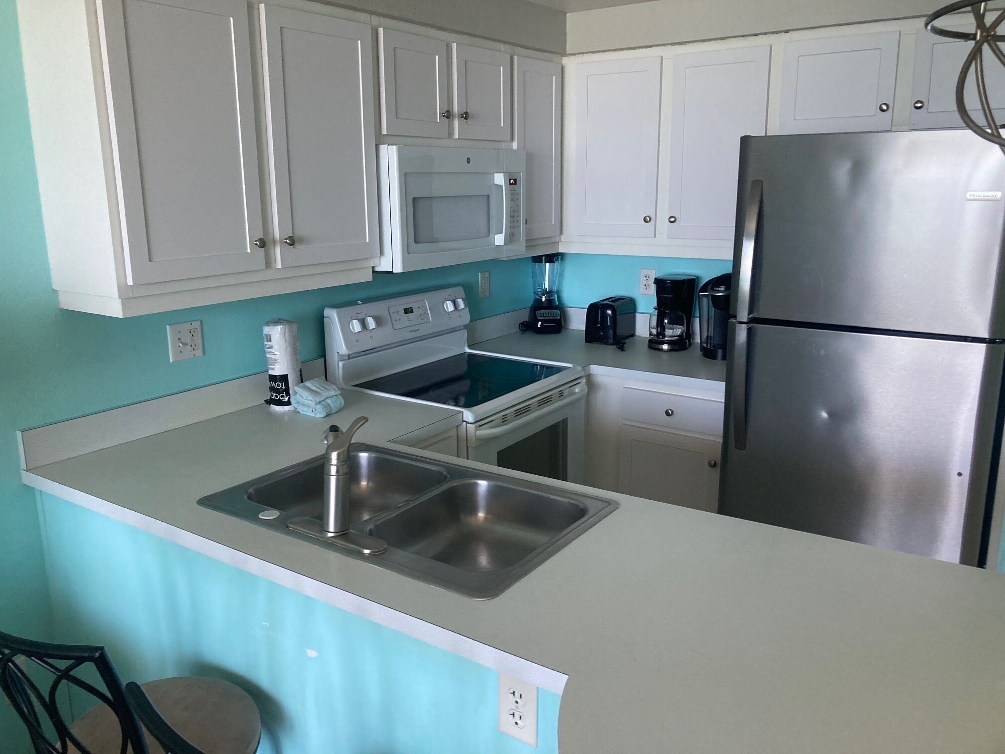 A kitchen with white cabinets, a stainless steel refrigerator, a stove, and a sink.