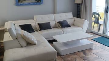 Een moderne woonkamer met een witte bank, een bijzettafeltje en een schilderij van een strand.