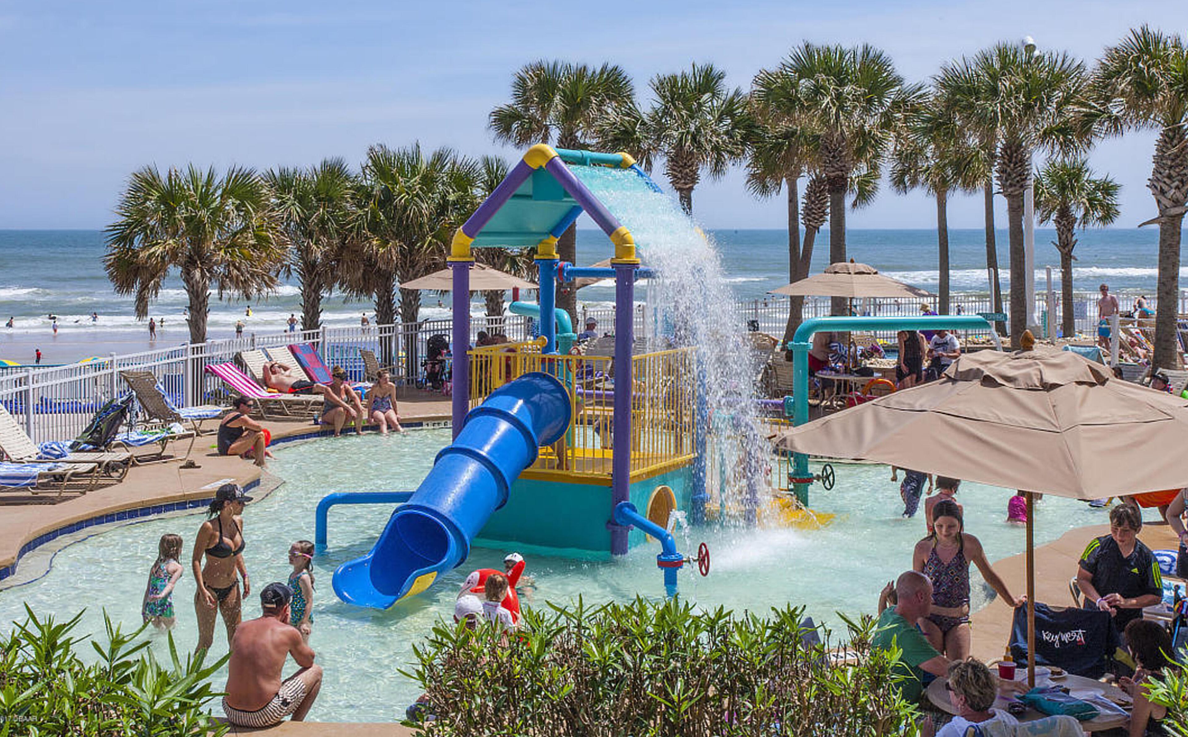 A water park with a blue slide, palm trees, and beach chairs.