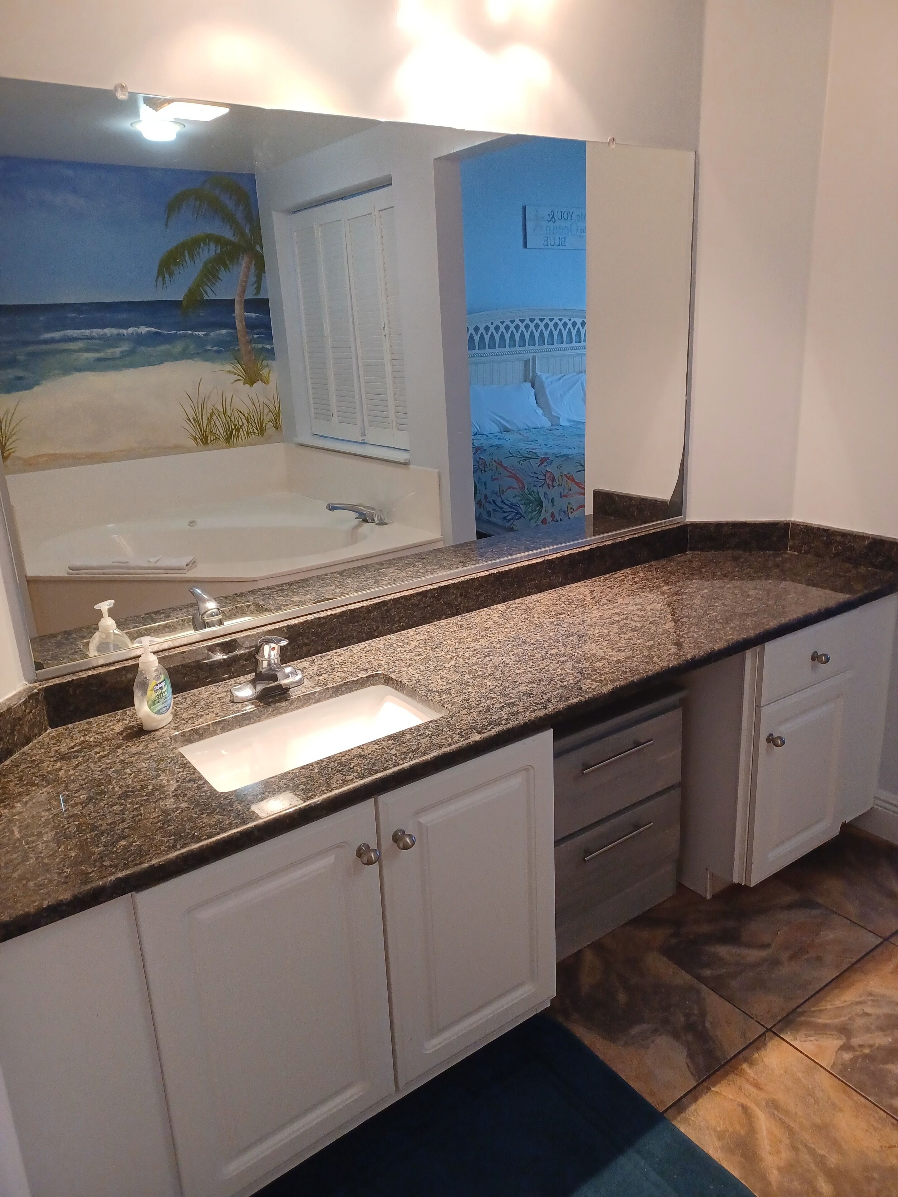 A bathroom with a large mirror, a bathtub, a sink with a soap dispenser, and a vanity with drawers.