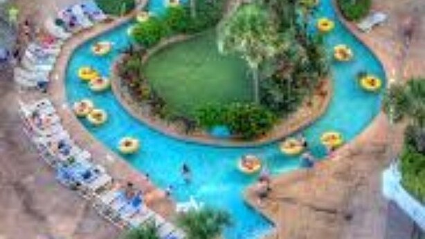 An aerial view of a resort with a large central pool, surrounded by palm trees and sun loungers. - Ocean Walk Resort (Daytona Beach)