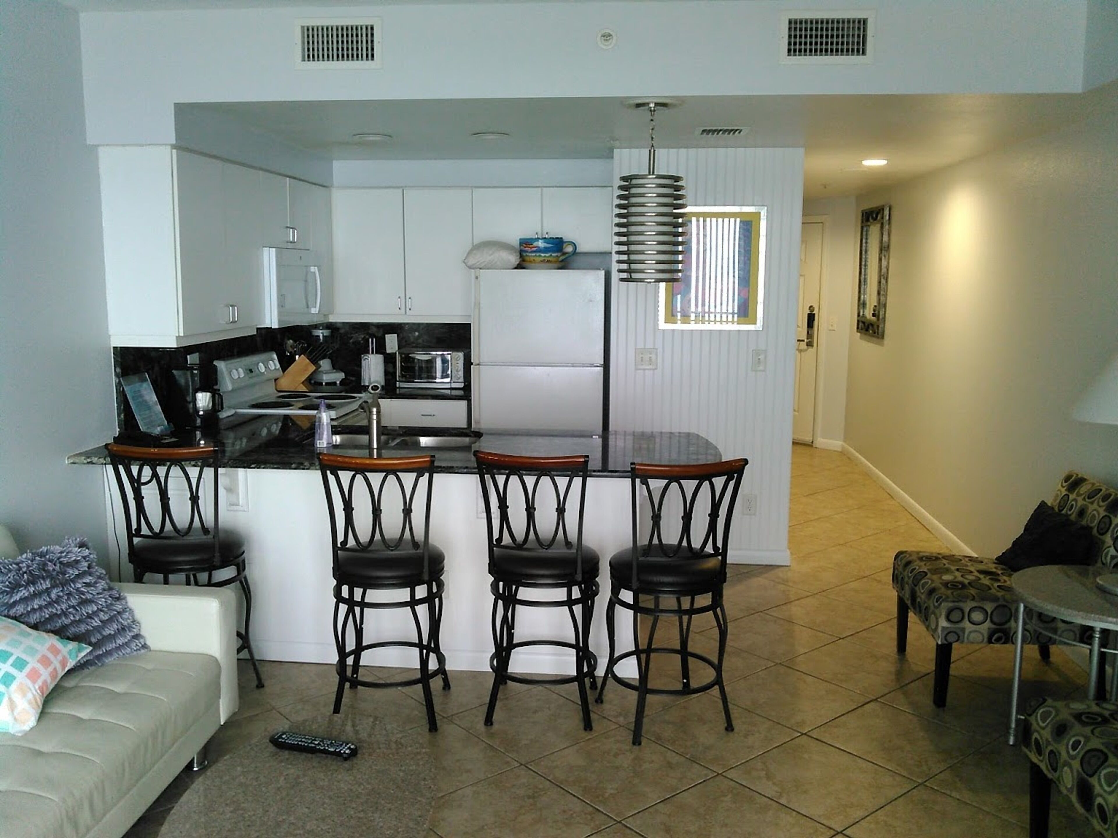 Cocina compacta con una isla central, taburetes de bar, un sofá y un pouf estampado.