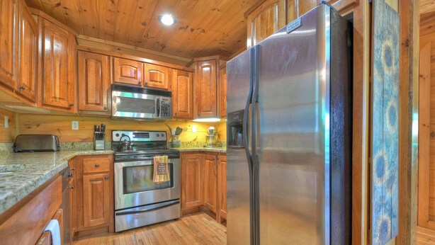 A kitchen with wooden cabinets, stainless steel appliances, and a granite countertop. - Logging Memories | Mtn Views + Hot Tub + Games (Blue Ridge)
