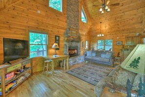 A log cabin interior with a fireplace, a television, and a sofa.