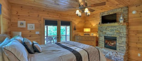 Un dormitorio de cabaña de madera con una cama, una chimenea de piedra, un televisor y un ventilador de techo.