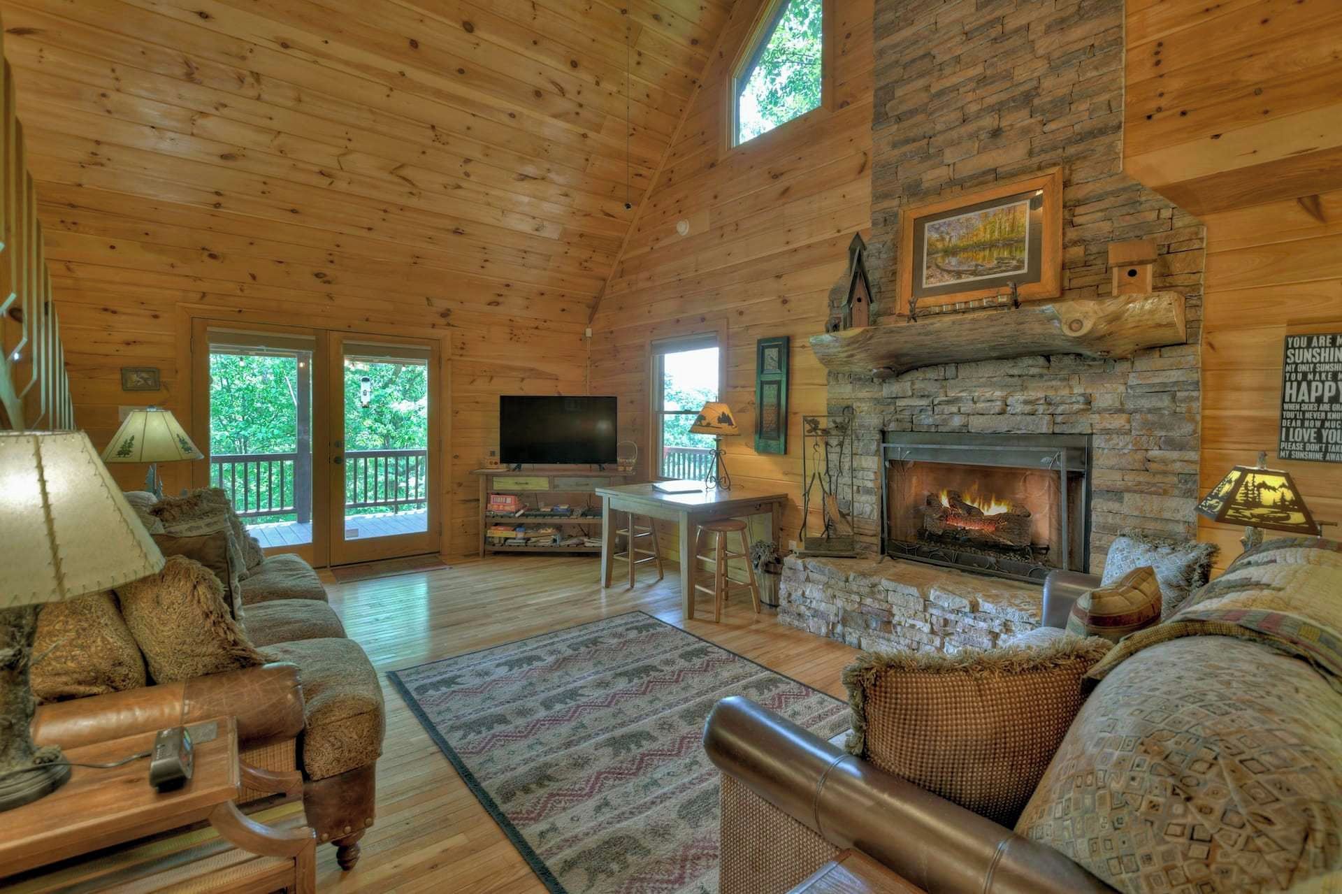 A cozy cabin interior with a stone fireplace, wooden walls, a television, and a sofa.