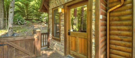A log cabin with a wooden deck, a stone wall, and a wooden door.