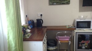A compact kitchen with a microwave, kettle, and a small table. There's a trash bin and a chair with a checkered tablecloth. A painting of birds and sheep hangs on the wall. - The Tackroom is a one bedroom Apartment just a short walk from Fanore Beach (Ballyvaughan)