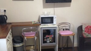 A compact room with a kitchenette, a microwave, a small refrigerator, a television, and a bed with a floral bedspread. - The Tackroom is a one bedroom Apartment just a short walk from Fanore Beach (Ballyvaughan)