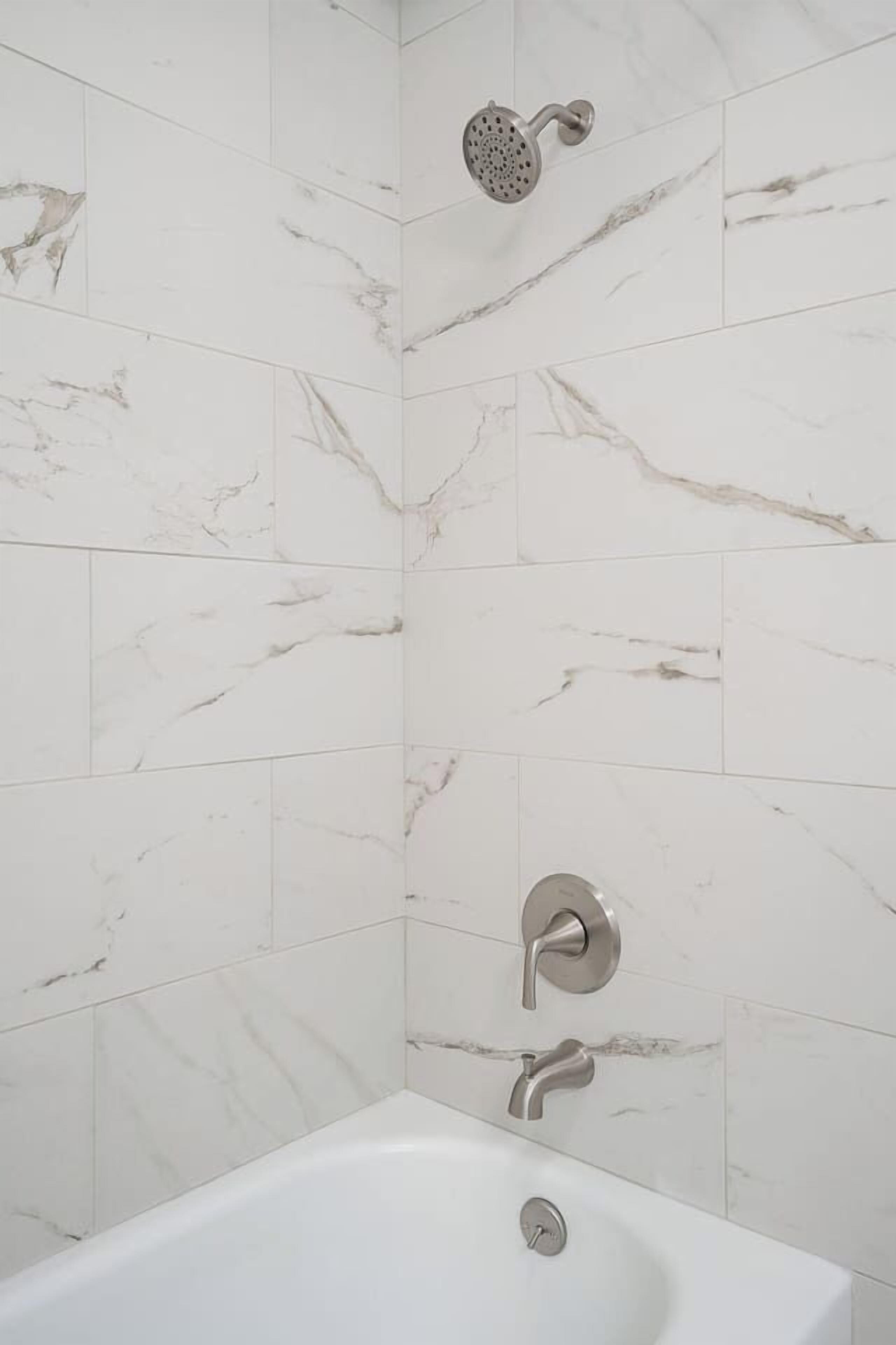 Un baño con zócalos de mármol blanco, una bañera y un cabezal de ducha.