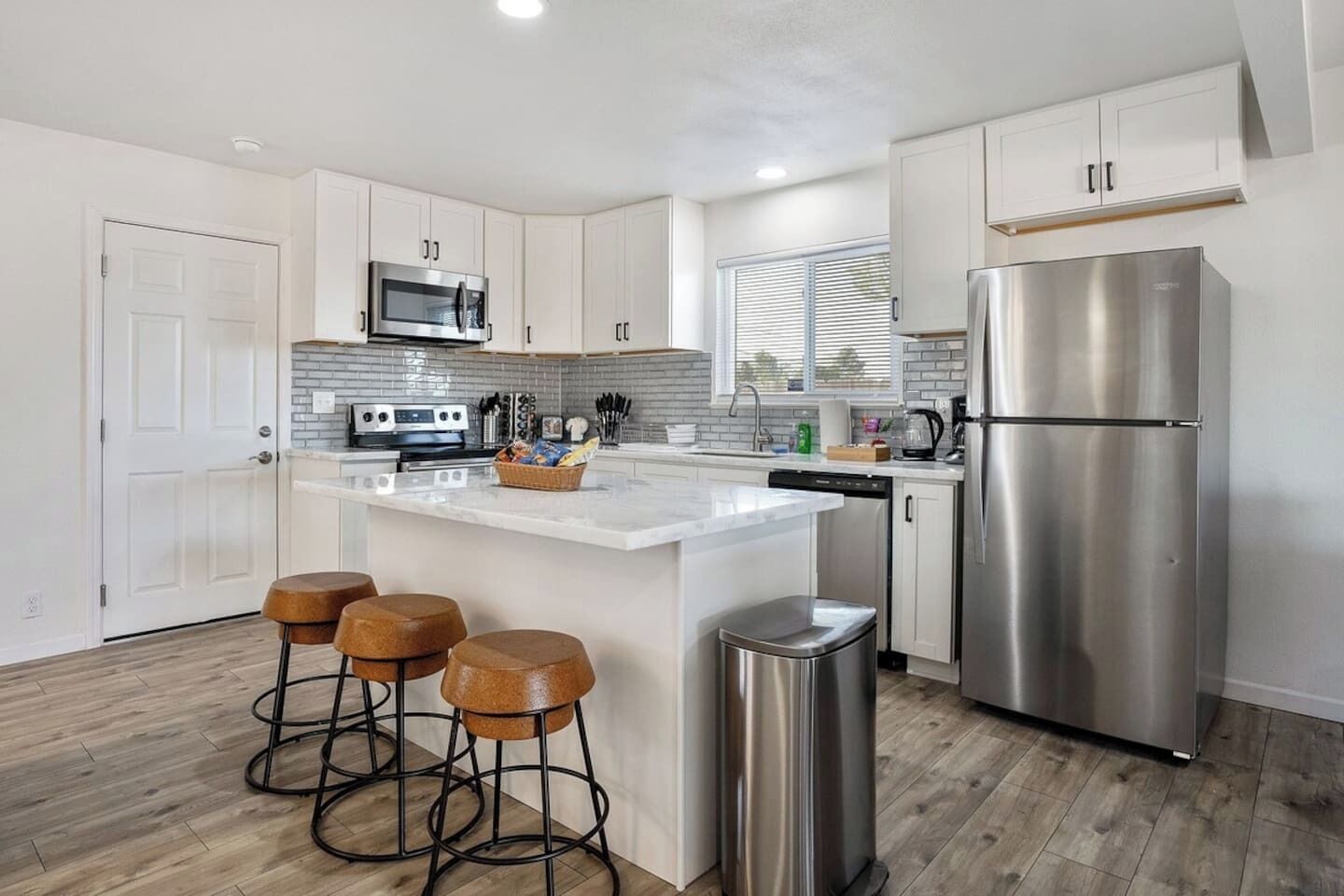 A modern kitchen with white cabinets, a stainless steel refrigerator, a microwave, and a central island with stools.