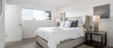 A bedroom with a large bed, a bedside table with a lamp, and a window with a view of trees.