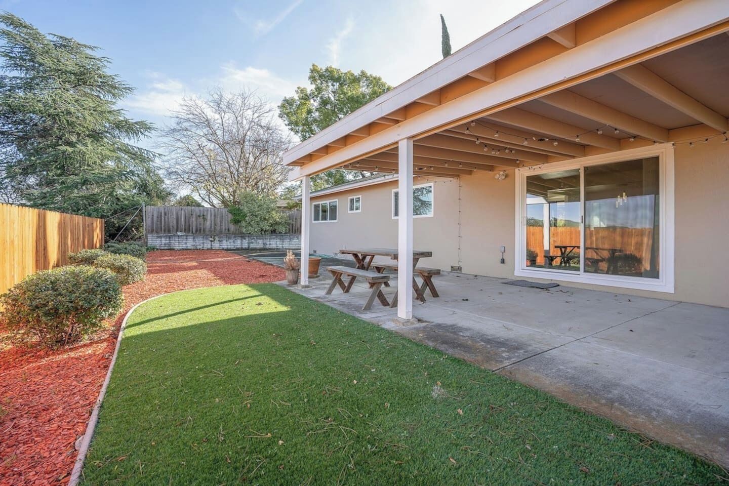 Una casa moderna con un porche cubierto, césped y valla de madera.