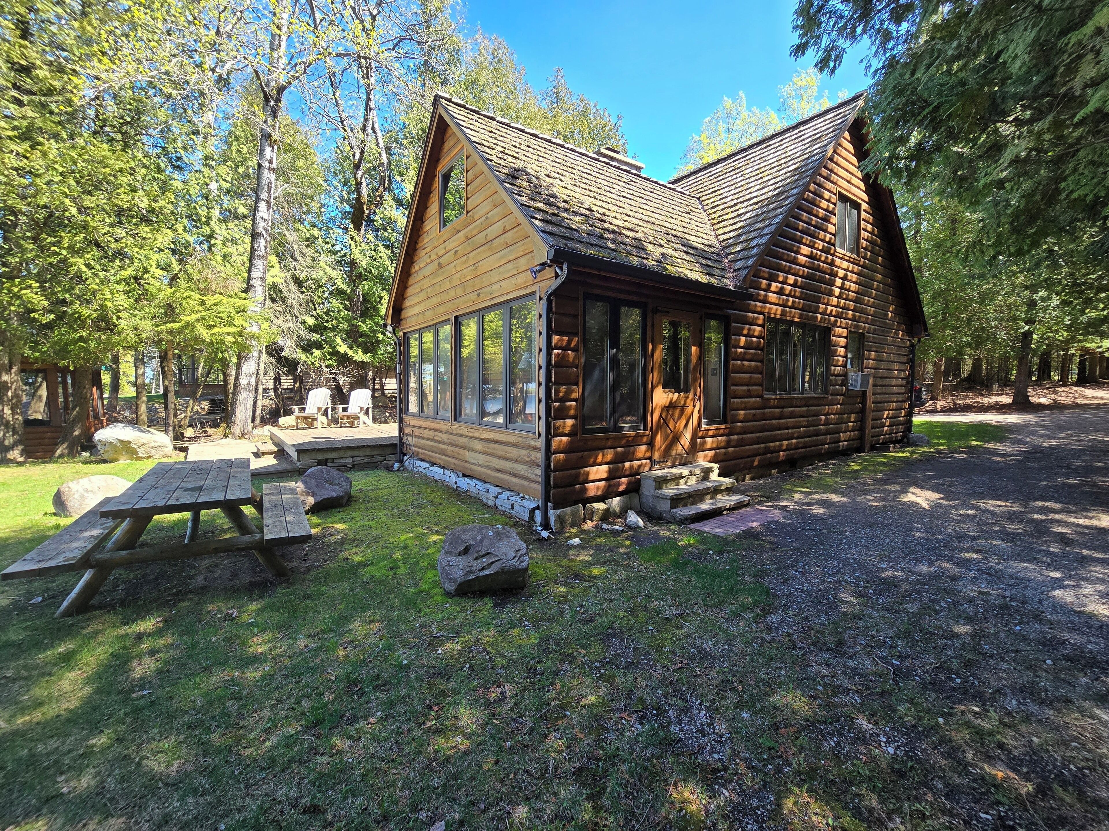 Una cabaña de troncos con terraza, mesa de picnic y ventanas amplias.